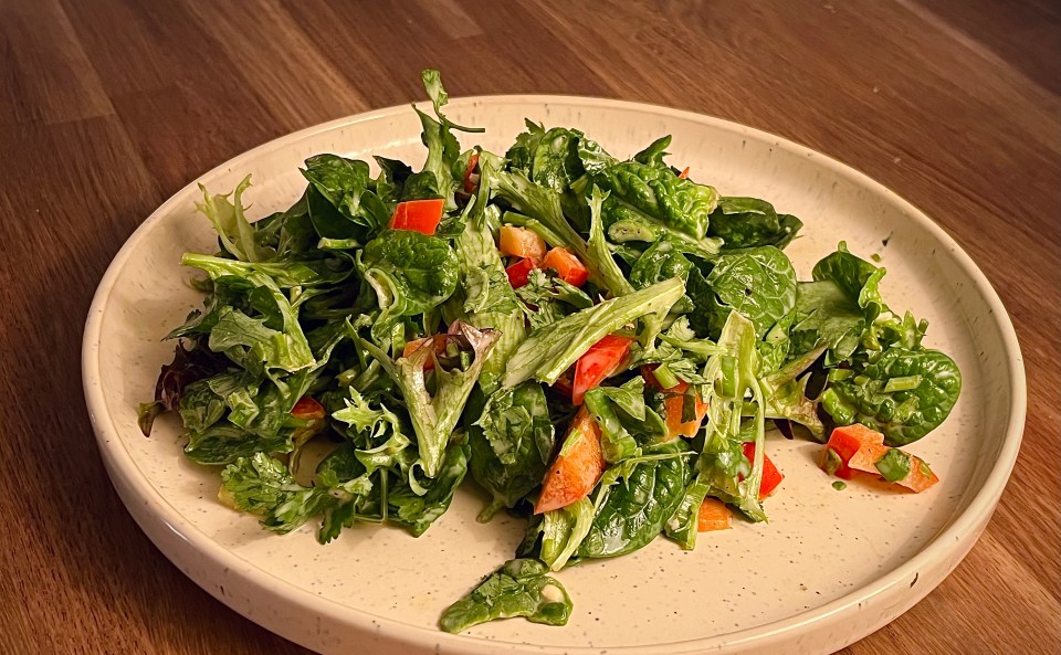 A leafy green salad toped with diced red peppers on a small beige plate on a dark wood table